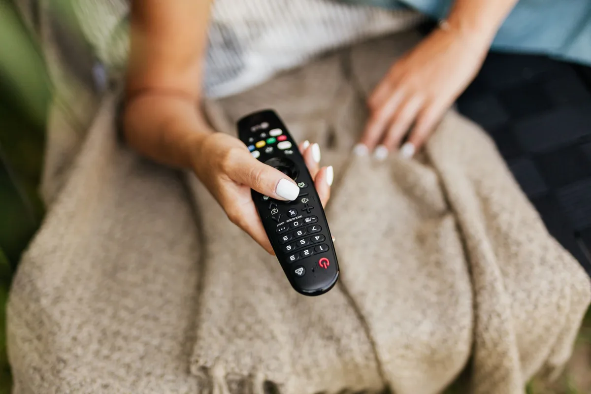 Mains tenant une télécommande devant un écran TV affichant les paramètres système