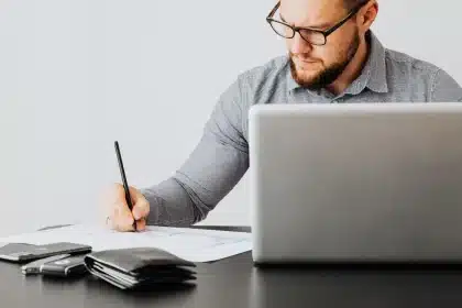 Mains manipulant des documents de paie et des feuilles de calcul sur un bureau avec un ordinateur portable affichant des