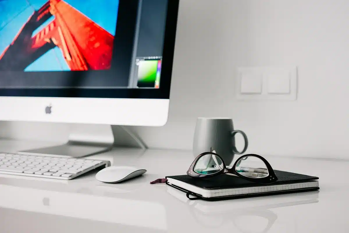 Bureau lumineux avec ordinateur affichant un schéma de workflow et mains anonymes prenant des notes