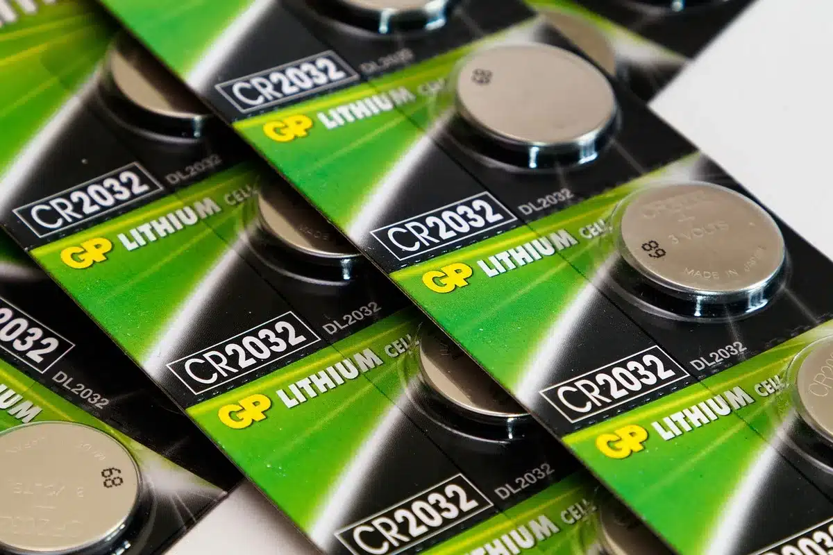 Mains gantées préparant des piles AA près d'une batterie de téléphone sur une table