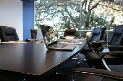 Table de réunion en plein jour, mains anonymes feuilletant des documents près d'un ordinateur portable