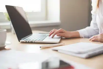 Bureau en journée avec ordinateur affichant un modèle d'invitation, checklist et fleurs