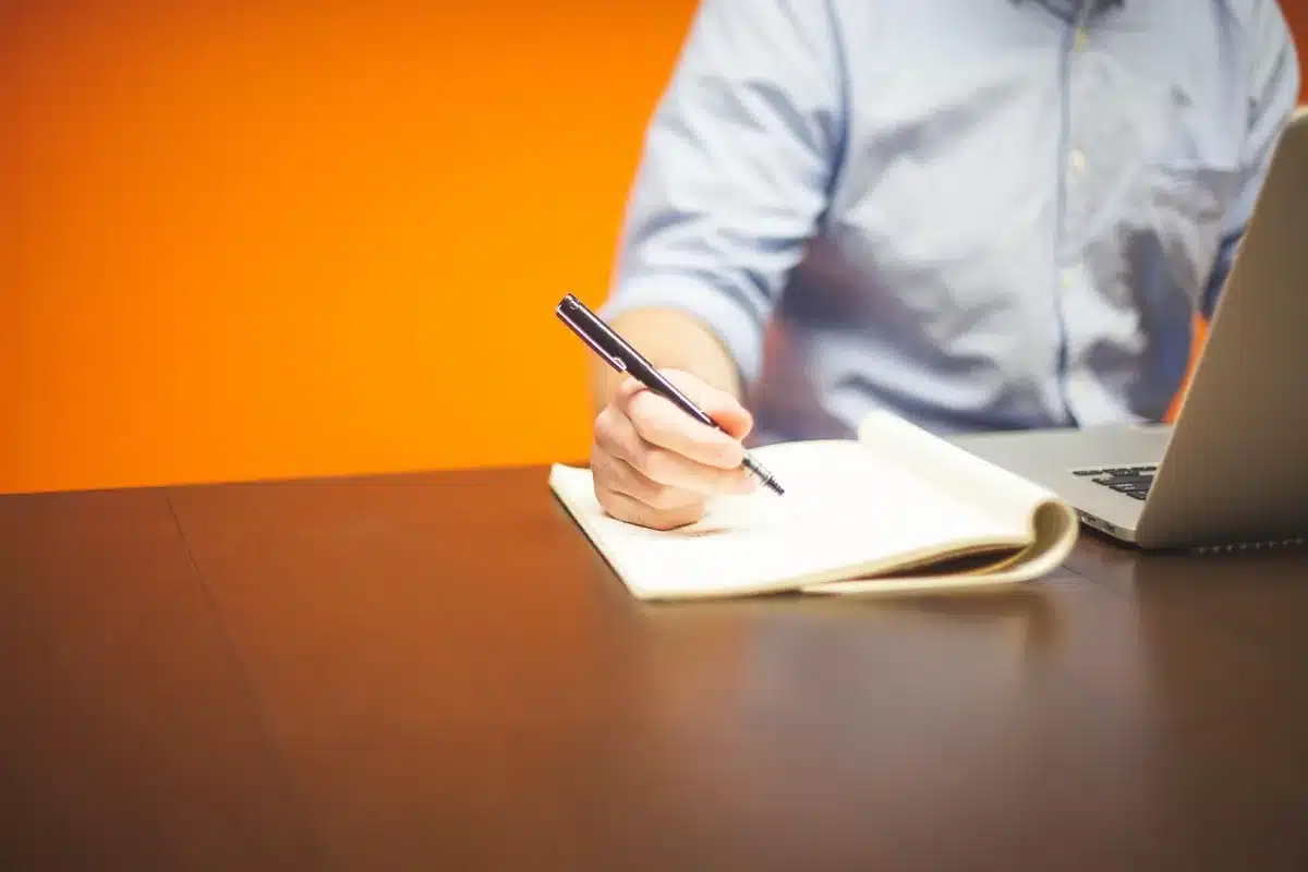 Bureau en journée avec ordinateur, carnet de séquences et tasse, évoquant l'email marketing