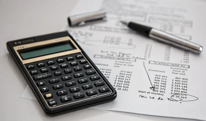 Maines manipulant des documents bancaires et une calculatrice sur un bureau en plein jour